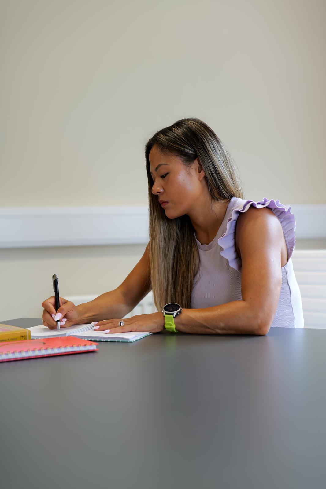 Betsy reflecting and writing in a notebook at a table